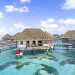 Overwater villa with couple in red dress in a tropical paradise setting.